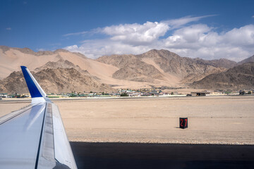 A shot from airplane window, visible plane wings. Dry Mountains with runway in the foreground and...