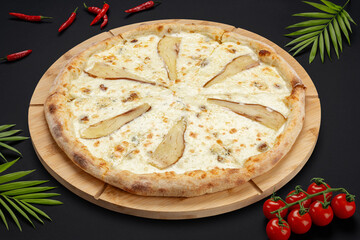 Pizza with cheese and pear on a round wooden board on a black background with tomatoes and peppers. Food photos. View from above.