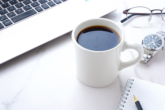 コーヒーを飲みながらノートパソコンでデスクワーク中のイメージ	
