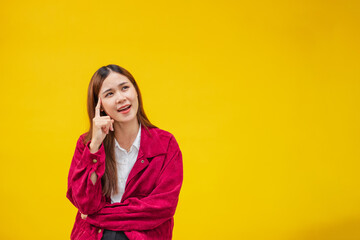 Smiling young Asian woman  thinking something over on  yellow wall background
