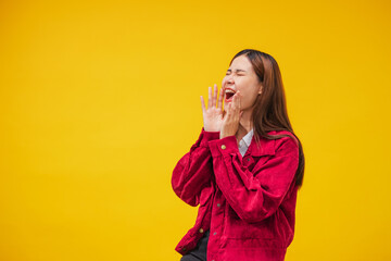 Smiling young Asian woman  shouting or annoucing something over on  yellow wall background