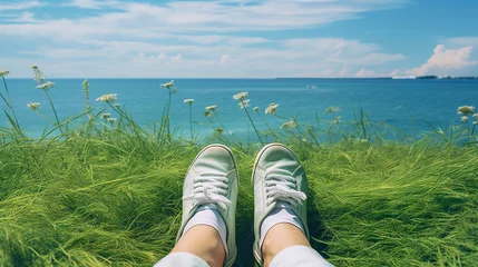 Tuinposter Leg with sneaker on grass while sitting near the ocean looking at scenery. © krung99