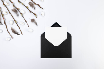 Top view of pussy willow branches, white easter eggs and feathers on white background. Black envelope, white card, post. Spring easter composition, copy space, flat lay.