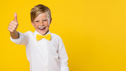 A happy boy wearing a white shirt and a yellow bowtie on a yellow background, gestures a thumbs-up gesture. Copy space