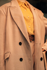 Close up details of a beige long coat and a bright yellow shirt. Casual stylish women's fashion