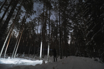 A man with a flashlight in the night forest in winter.