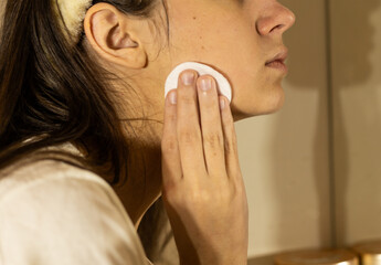 teenage girl wipes her face with a cotton sponge with tonic