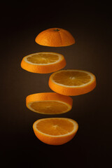 sliced fresh orange floats freely on a dark brown soft background with a gradient spot of light. artistic moody vertical closeup photo with soft lighting. selective focus