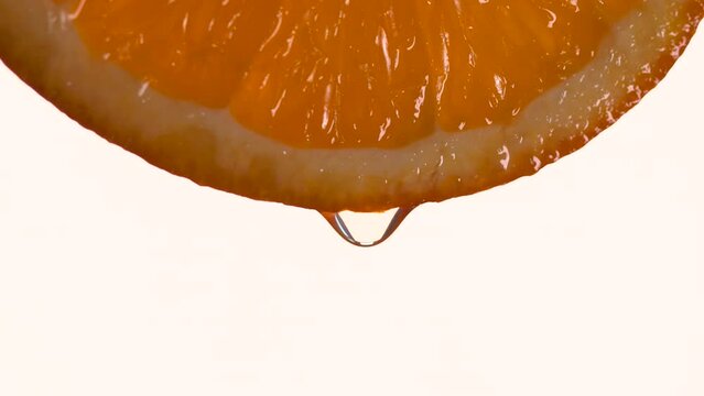 Juice drop slowly falling from orange full of nutrients and vitamins. Close up of juicy orange slice on a white background.