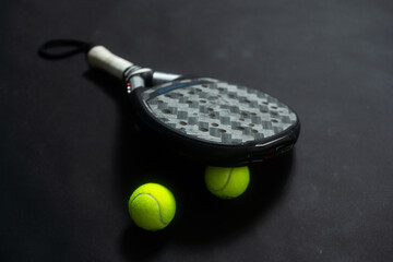 Detailed background of black and white padel racket and ball on black background. Top view.