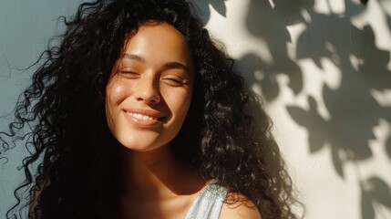 Smiling woman with long curly hair against a wall with tree shadow.