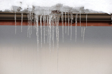 Shiny icicles hanging from the roof of the house, sunny weather, snow on the roof