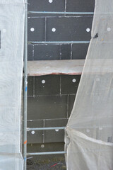 A wall of a house covered with EPS graphite polystyrene boards for thermal insulation, a scaffolding and building safety scaffolding net, anchors
