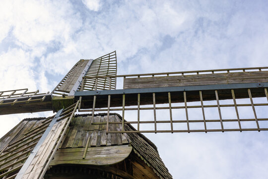 The wings of an ancient wooden mill are photographed from below against a blue sky background.