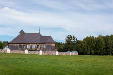 An old wooden Catholic church with a stone fence in the distance near the forest. Lithuania Rumsiskes