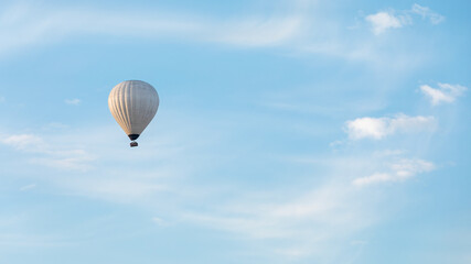 White hot air balloon flying in a blue sky with white clouds
