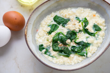 Bowl of stracciatella soup or egg-drop soup with spinach, horizontal shot on a light-beige marble surface, middle closeup