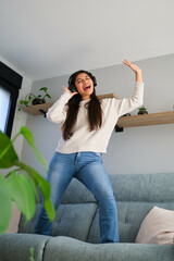 Female teenager with braces dancing and singing on the sofa listening to music with headphones.