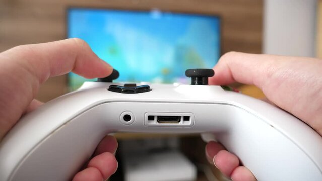 Teenager hands hold playing portable gamepad joystick console game on TV at home