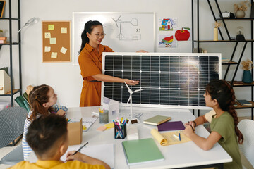 Positive teacher showing children solar panel and explaining how it works