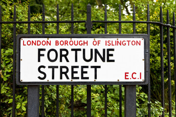 Street sign for a road called Fortune Street, with wrought iron railings and foliage background....