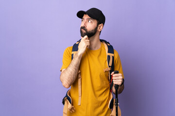 Caucasian handsome man with backpack and trekking poles over isolated background having doubts and...