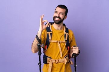 Caucasian handsome man with backpack and trekking poles over isolated background showing ok sign with fingers