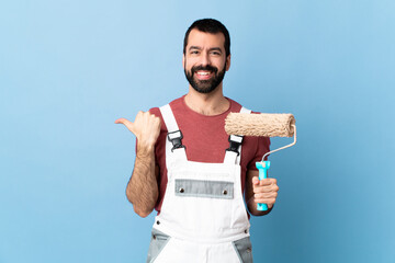 Adult painter man over isolated blue background pointing to the side to present a product