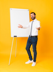 Full-length shot of businessman giving a presentation on white board over isolated yellow background presenting and inviting to come with hand