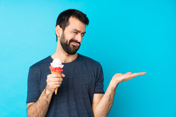 Young man with a cornet ice cream over isolated blue background holding copyspace with doubts