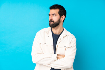 Young handsome man with white corduroy jacket over isolated blue background with confuse face...