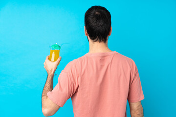 Young man over holding a cocktail over isolated blue background in back position