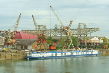 Fototapeta na wymiar Industrial River Scene With Blue Cargo Barge and Cranes on an Overcast Day