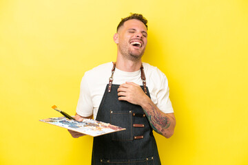 Young artist caucasian man holding a palette isolated on yellow background smiling a lot
