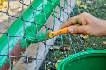 Obraz premium Cropped hand of man painting green color on chainlink fence