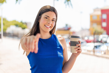 Young pretty Brazilian woman holding a take away coffee at outdoors points finger at you with a confident expression