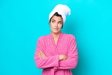 Young Brazilian woman with a bathrobe isolated on blue background making doubts gesture while...