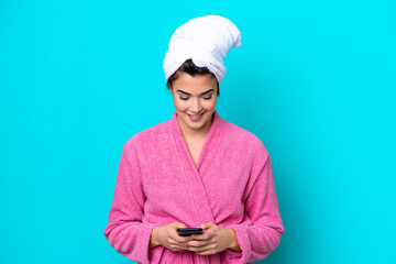 Young Brazilian woman with a bathrobe isolated on blue background sending a message with the mobile