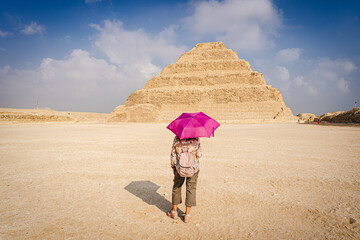 Cairo, Egypt - October 26, 2022. View of a woman with a purple umbrella watching the scale pyramid of Djoser in the Saqqara necropolis. - 745071295