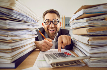 Funny smiling happy business man in suit and glasses working at the desk on his workplace at office...