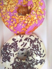 Picture of assorted donuts in a box with chocolate frosted, pink glazed and sprinkles donuts.