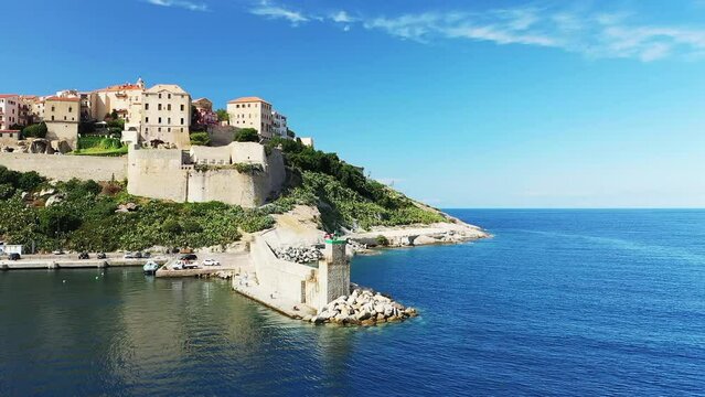 The lighthouse at the entrance to the port of the city of Calvi and its medieval fort , in Europe, France, Corsica, by the Mediterranean Sea, in summer, on a sunny day.