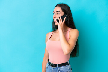 Fototapeta premium Young caucasian woman isolated on blue background keeping a conversation with the mobile phone with someone