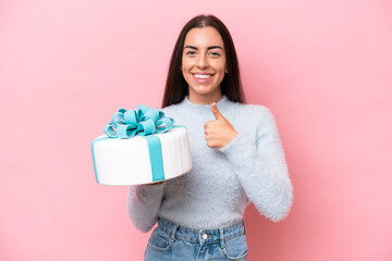 Young caucasian woman holding birthday cake isolated on pink background giving a thumbs up gesture