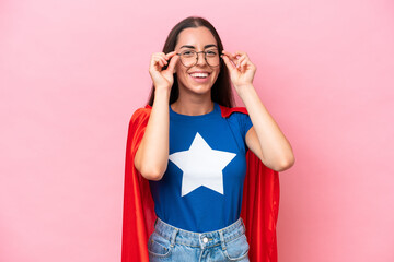 Super Hero Caucasian woman isolated on pink background with glasses and surprised