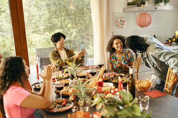 Cheerful man making photo on phone for smiling friends during festive home party
