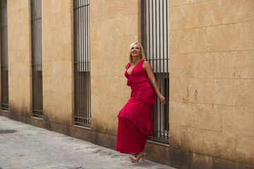 Beautiful blonde mature woman in an elegant dress leaning against the wall of a building on a narrow street in a town in Andalusia, Spain.