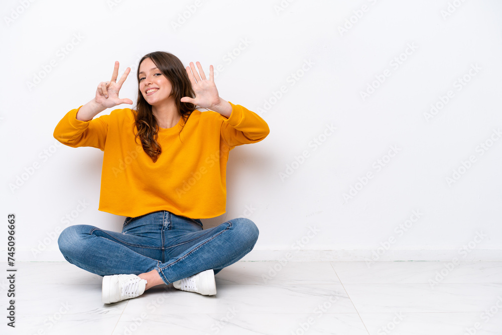 Wall mural Young caucasian woman sitting on the floor isolated on white wall counting eight with fingers