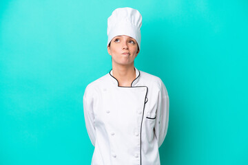 Young caucasian chef woman isolated on blue background and looking up