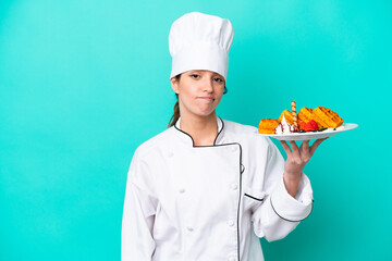 Young caucasian chef woman holding waffles isolated on blue background with sad expression